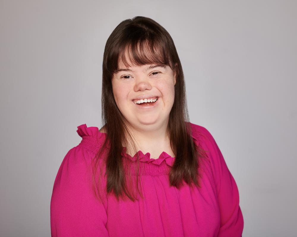 Charlotte Woodward 2023 headshot. Wearing a pink shirt smiling at the camera