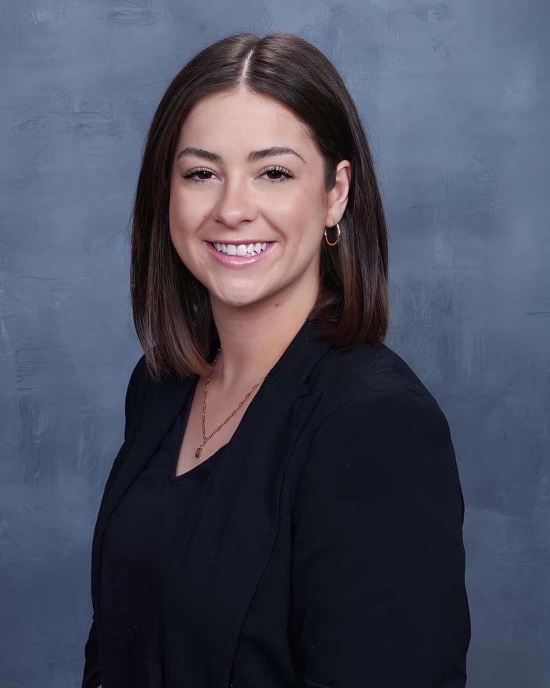 genevieve thompson headshot wearing a black blazer, black shirt and her brown hair is shoulder length