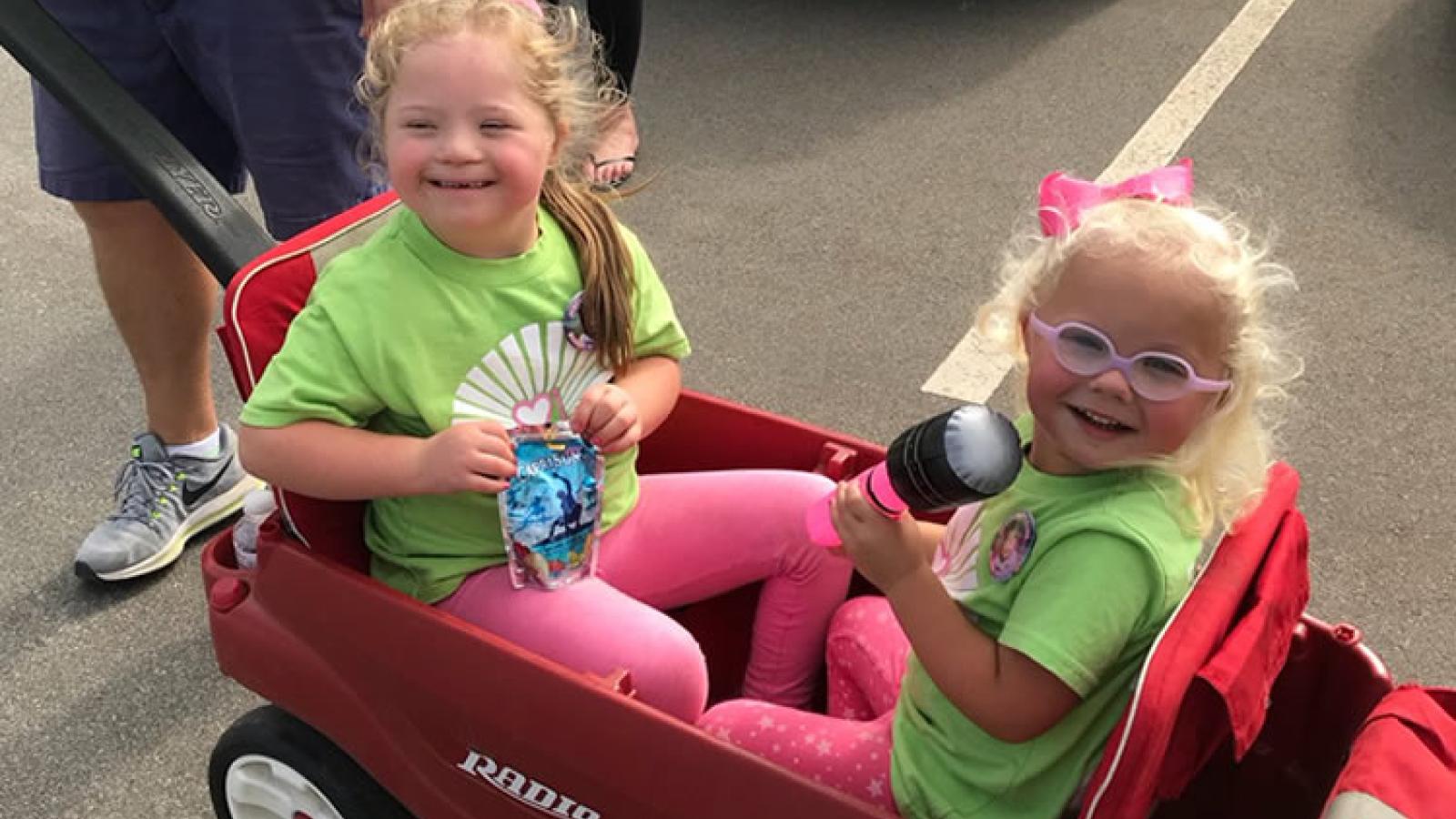 Two young girls sit in a wagon.