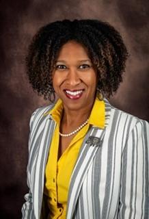 Woman with yellow button down and grey and white striped blazer smiling in headshot