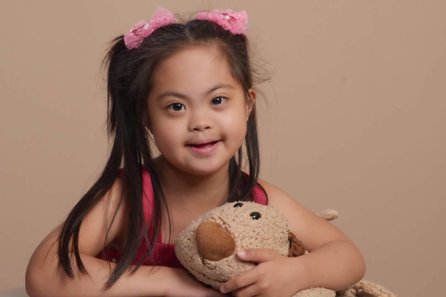 Girl with Down syndrome smiles and holds her stuffed animal