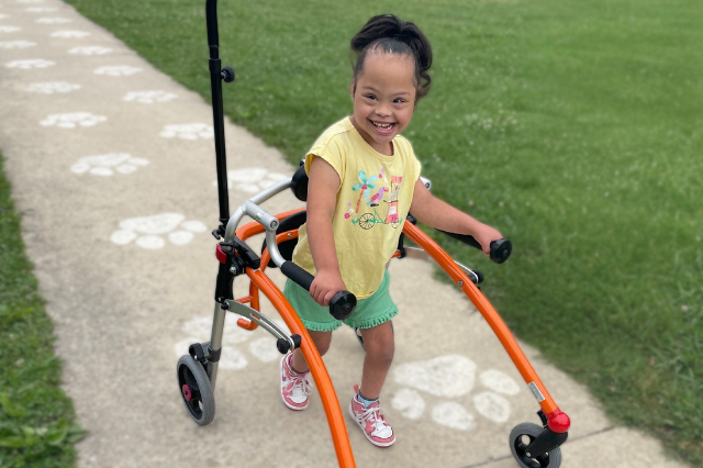 Girl with Down syndrome smiles while using an orange walker