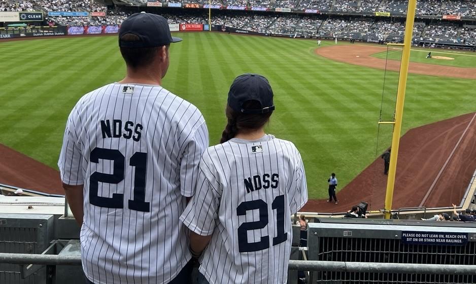 Two people looking out at the Yankees stadium. The back of there jerseys have the number 21 and say NDSS